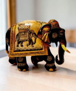 Carved wooden elephant figurine with hand-painted Indian ceremonial details on a tabletop.