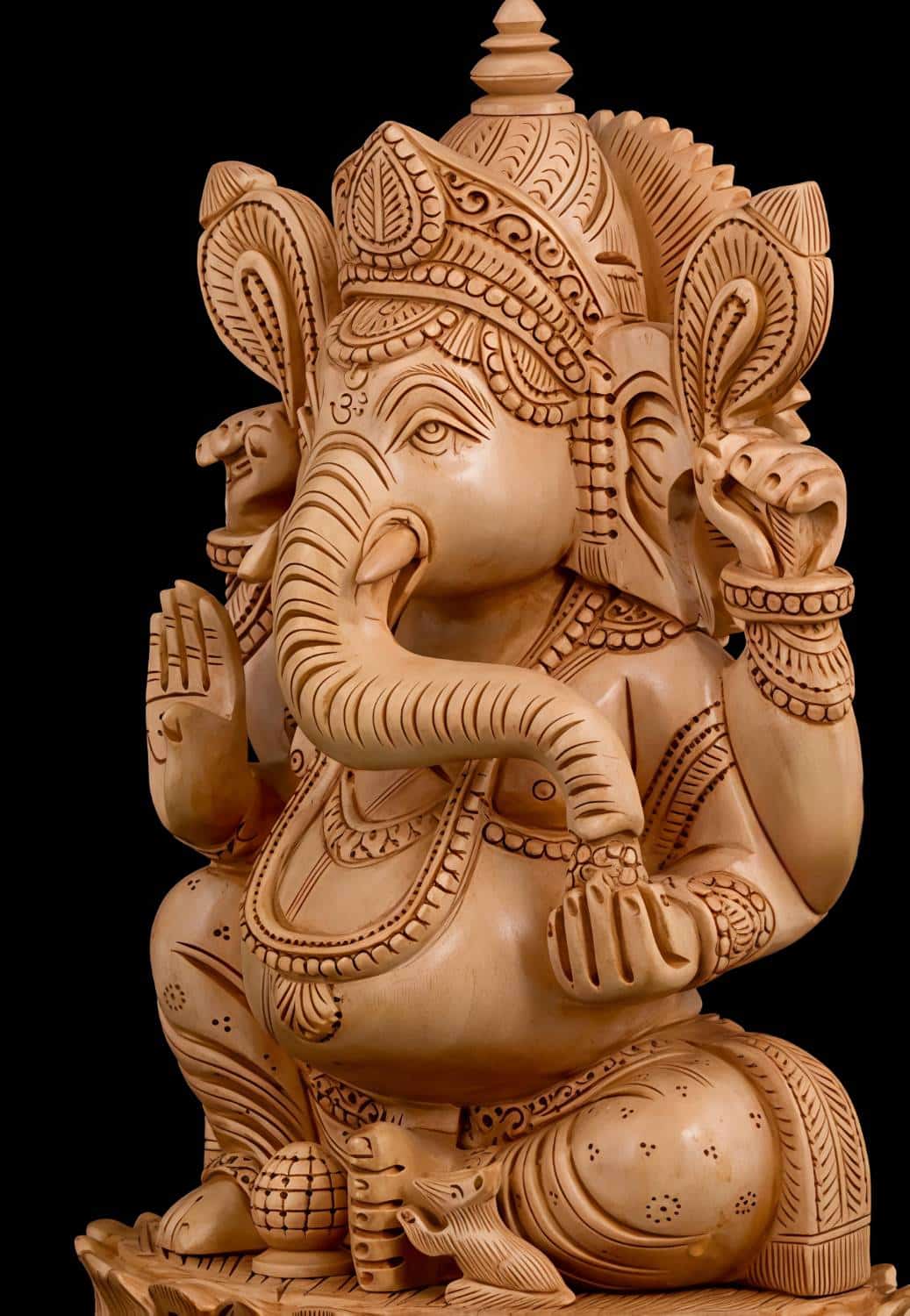 Intricately carved wooden Ganesha statue with ornate crown and blessing gesture.