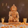 Wooden Hanuman ji statue with intricate carvings, flower petals, incense, and ceremonial offerings in a spiritual setting.