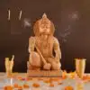 Wooden Hanuman ji statue with intricate carvings, flower petals, incense, and ceremonial offerings in a spiritual setting.