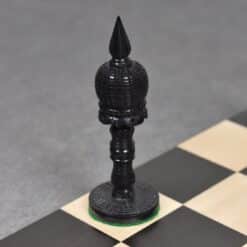 Black ornate bishop chess piece on wooden board with other pieces in background.