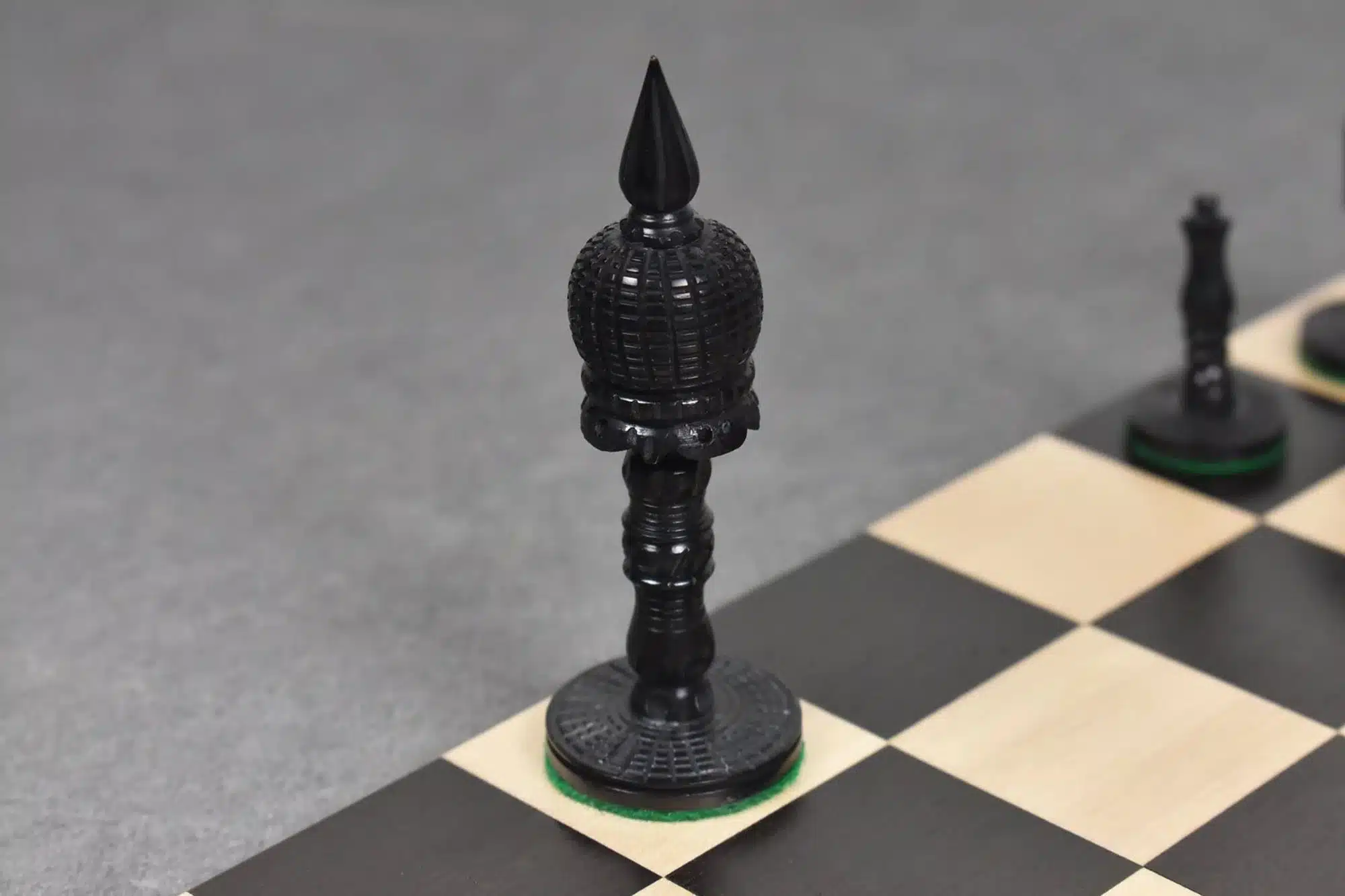 Black ornate bishop chess piece on wooden board with other pieces in background.