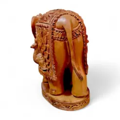 Ornate carved wooden elephant figurine with ceremonial saddle on decorative base.
