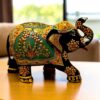 An ornate painted elephant statue with gold and green details on a wooden table.