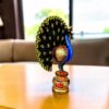 An ornate hand painted wooden peacock figurine resting on a polished table.
