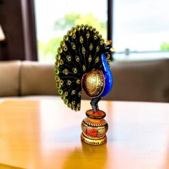 An ornate hand painted wooden peacock figurine resting on a polished table.